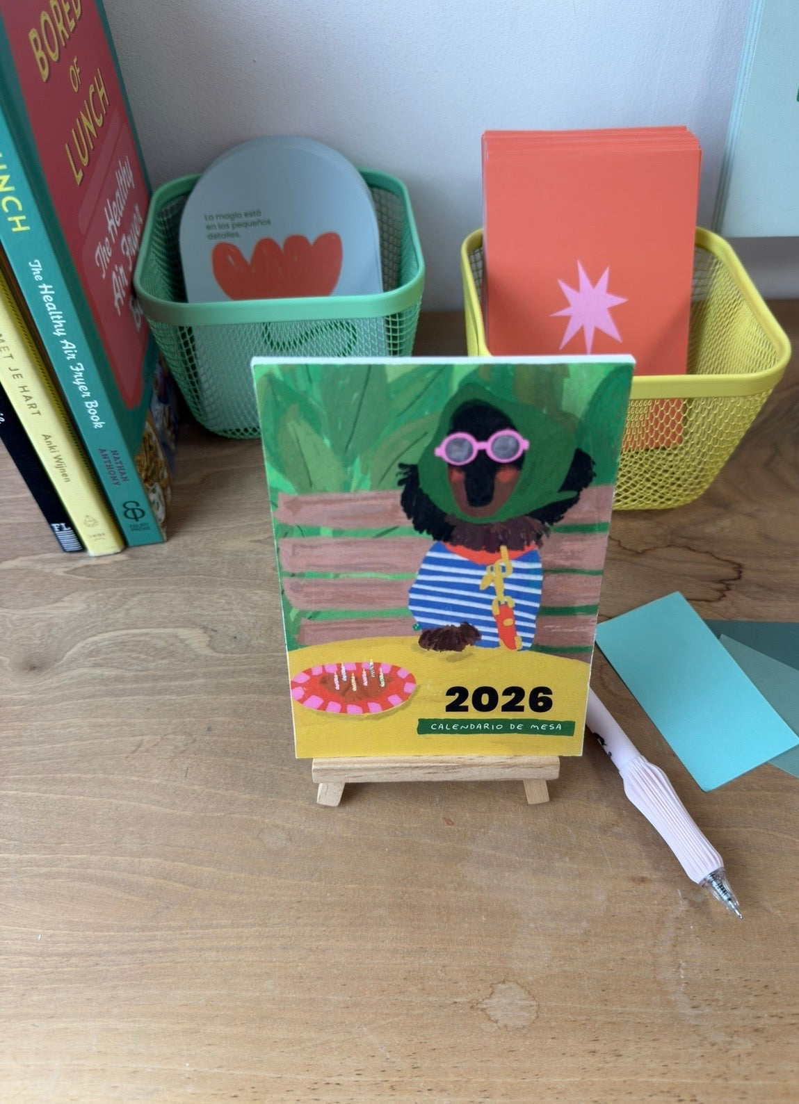 Calendario ilustrado 2026 de Alejandra Lozano en formato A6 sobre caballete de madera. Arte colorido y minimalista para decorar el escritorio con estilo y serenidad.