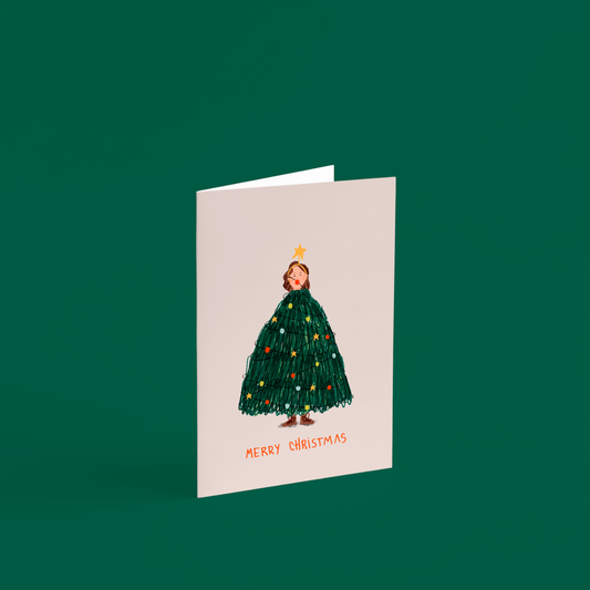 Tarjeta ilustrada “Merry Christmas” de Alejandra Lozano, con una mujer vestida de árbol de Navidad. Diseño artístico navideño con sobre kraft, estilo natural y tierno.